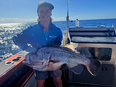 A smiling boy on a boat holds a large fish.