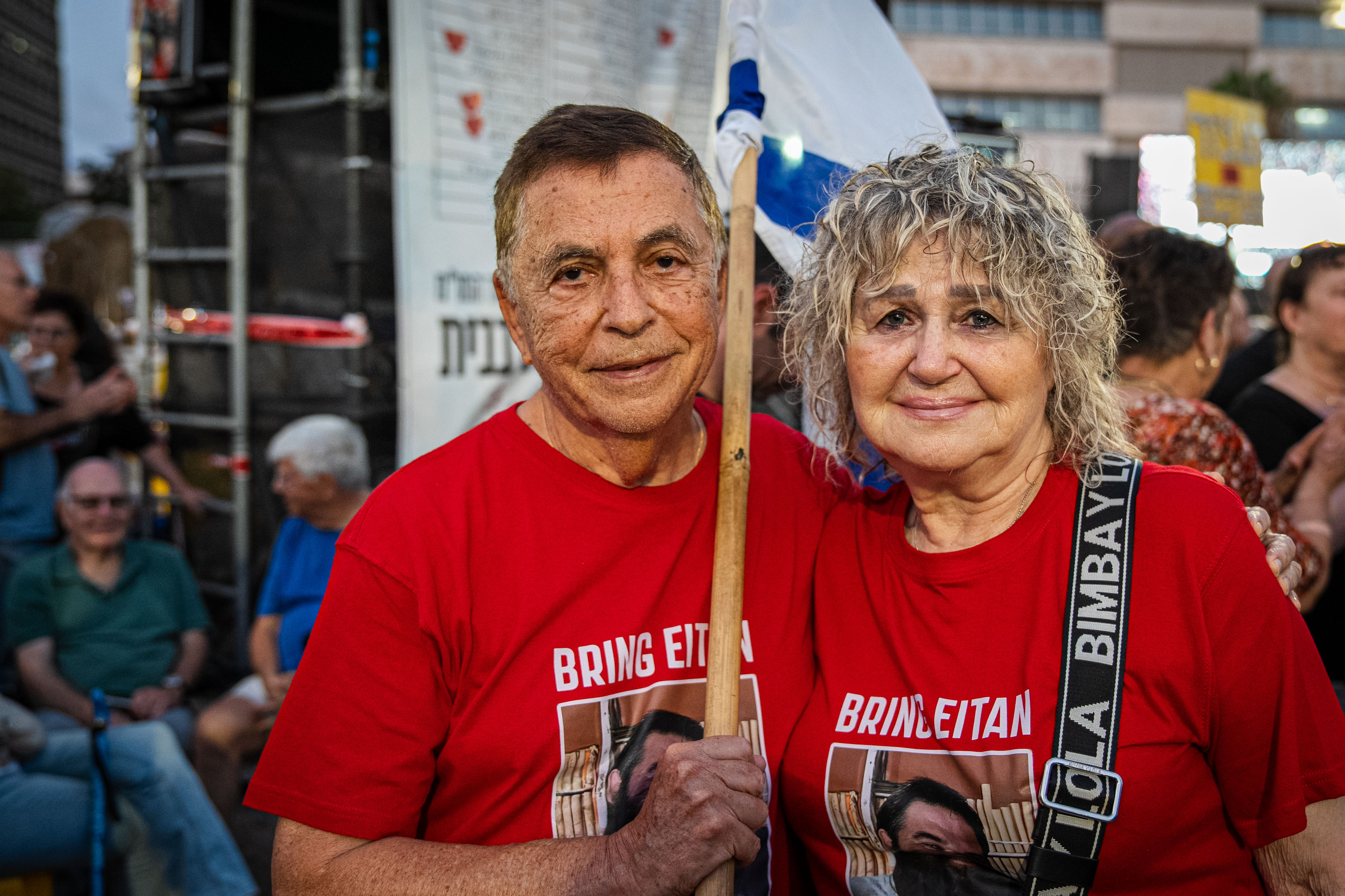 A man and woman hugging wearing a t-shirt with a photo of a hostage reading Bring Eitan home