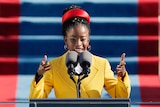 A woman wearing a bright yellow coat and red headband delivers a speech on the steps of the US Capitol