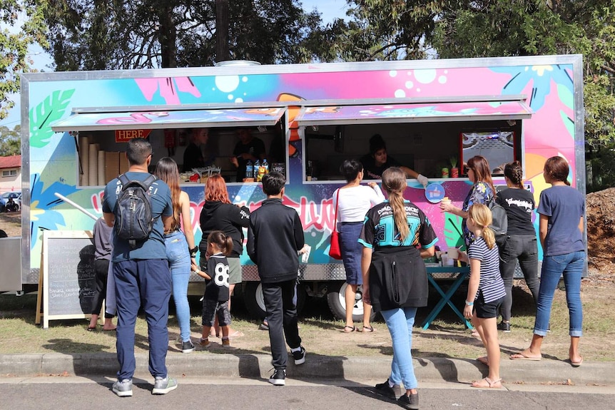 Crowd of customers line up to buy food from the Good Grub Food van.