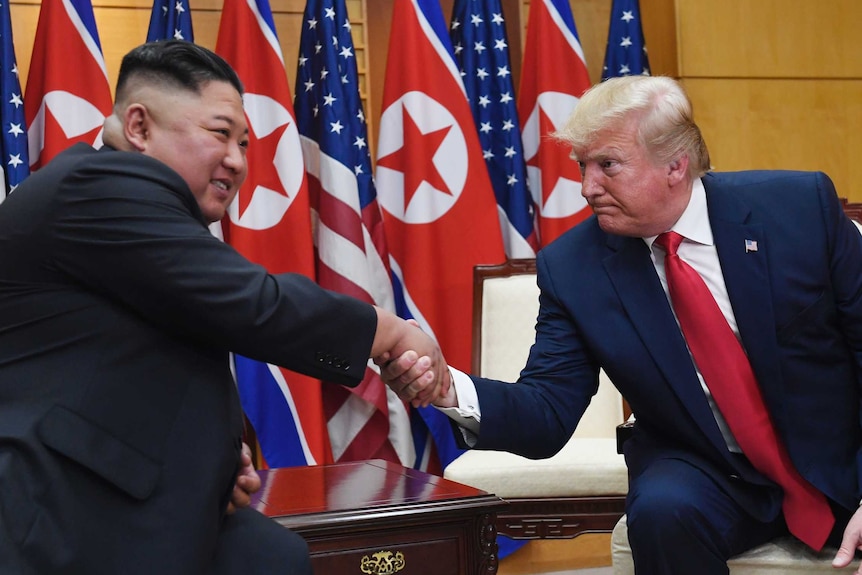 Kim Jong-un (left) shakes hands with Donald Trump as the pair sits in chairs with North Korean and US flags behind them.