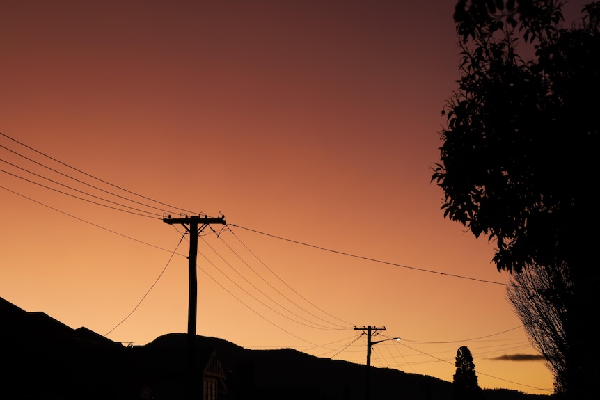 Silhouette of power poles and wires against an orange sky
