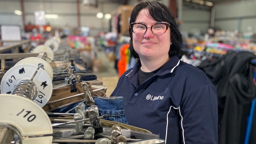 A woman with black hair, glasses, and a lifeline polo sorts a clothing rack 