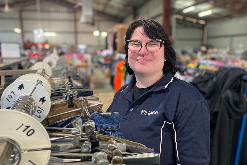 A woman with black hair, glasses, and a lifeline polo sorts a clothing rack 