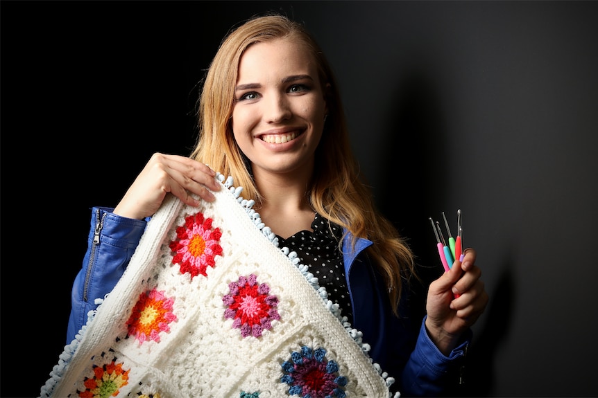 Annalivia Keaveny holds a crocheted blanket with her crochet hooks.
