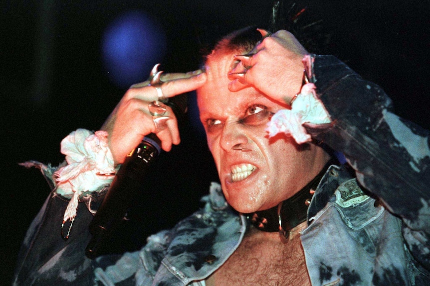 Keith Flint on stage wearing a denim jacket and lots of silver spiky rings and a spiked black collar