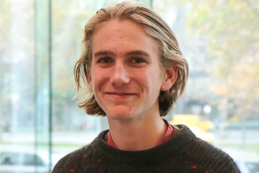 A teenage boy wearing a woollen jumper looks at the camera, smiling.