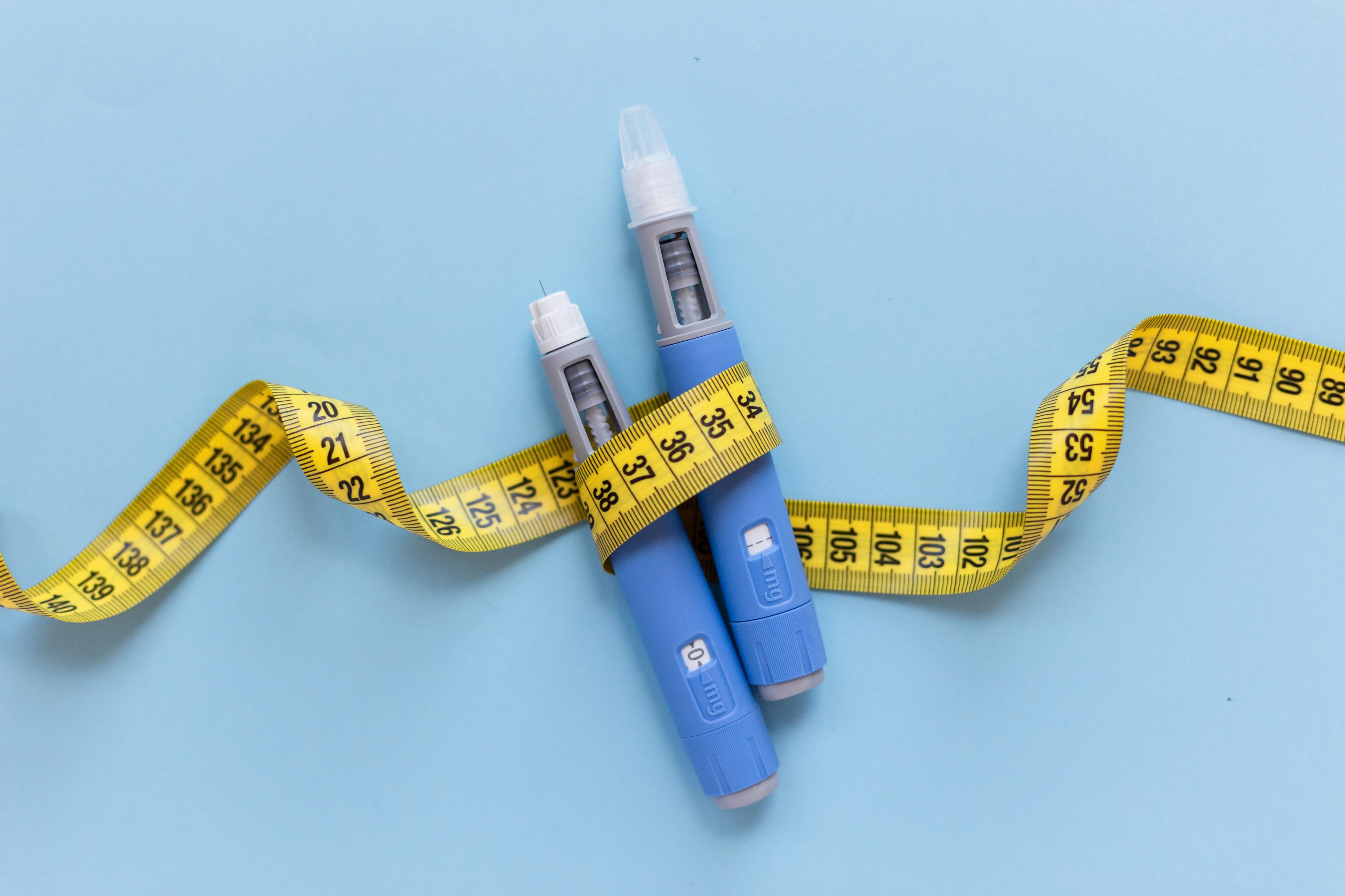 Two dosing pens for subcutaneous injection of anti-obesity medication, with yellow measuring tape around them