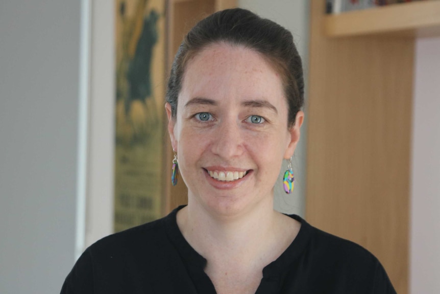 Katie Brooks smiles at the camera with brown hair and colourful earrings.