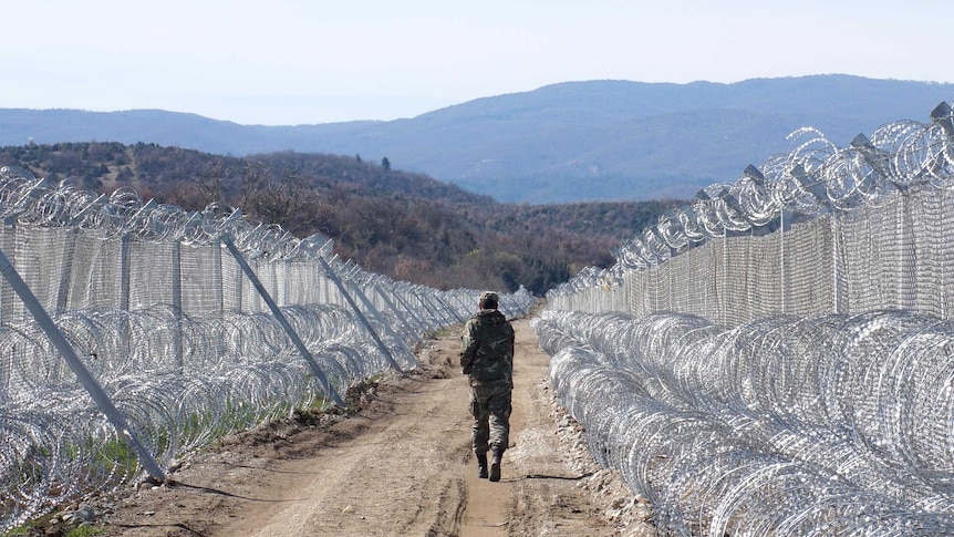 A lone member of the Macedonian army walks away from the camera as he patrols the razor wire border fence.
