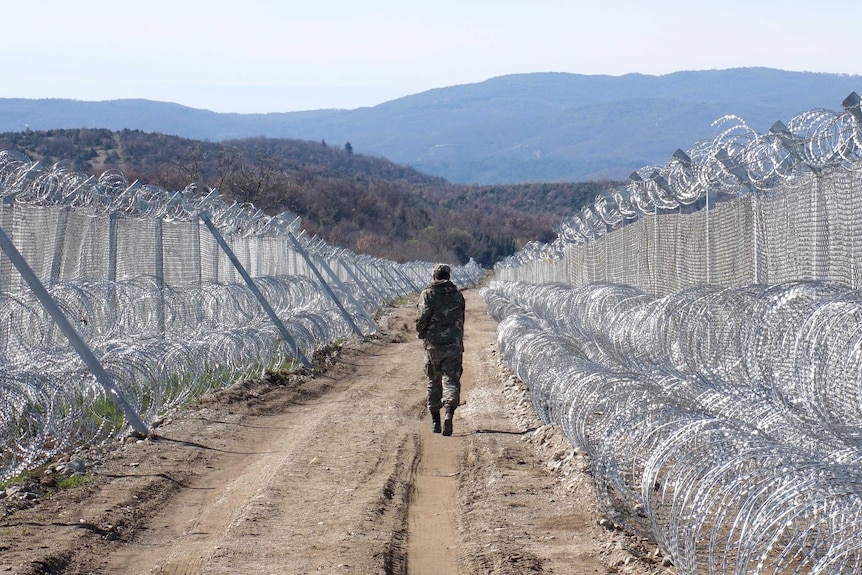 A lone member of the Macedonian army walks away from the camera as he patrols the razor wire border fence.