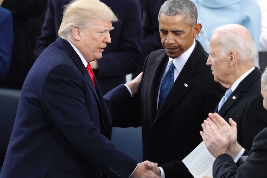 Joe Biden holding the hand of Donald Trump while Barack Obama looks down