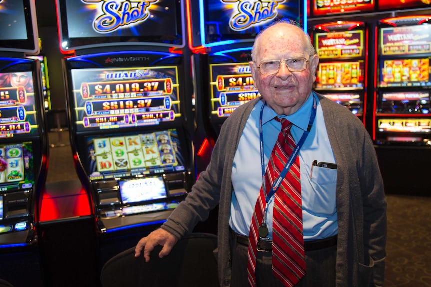 Len Ainsworth smiles as he stands in front of a row of flashing Ainsworth Quad Shot poker machines.