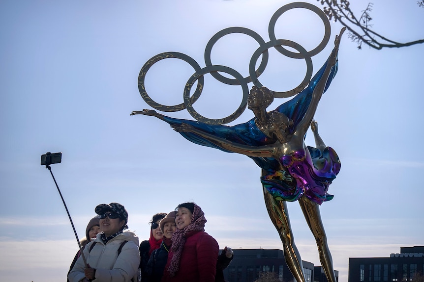 Visitors pose for a selfie with a statue containing the Olympic rings.