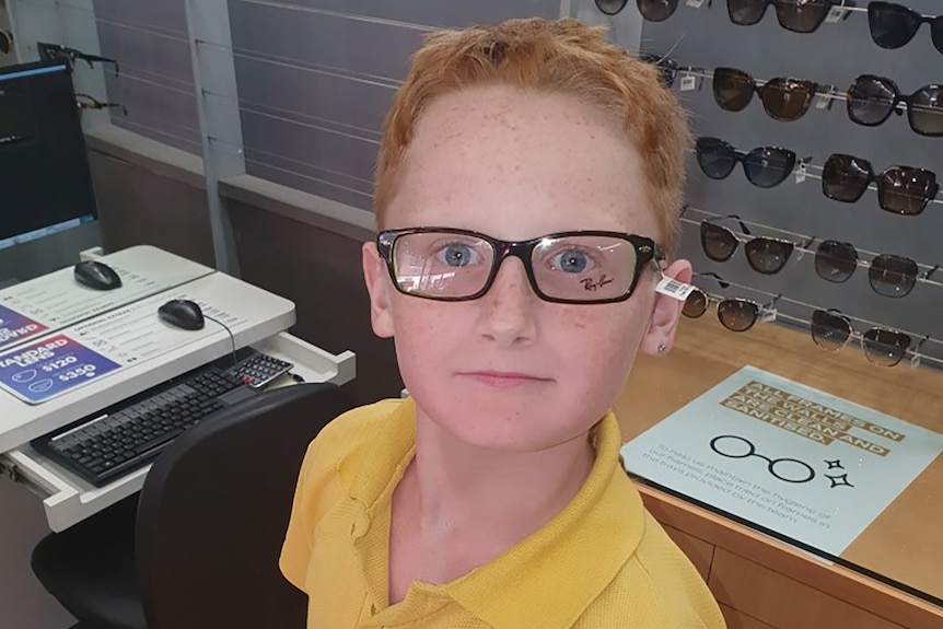 A young boy with orange hair wearing glasses in an optometrist store