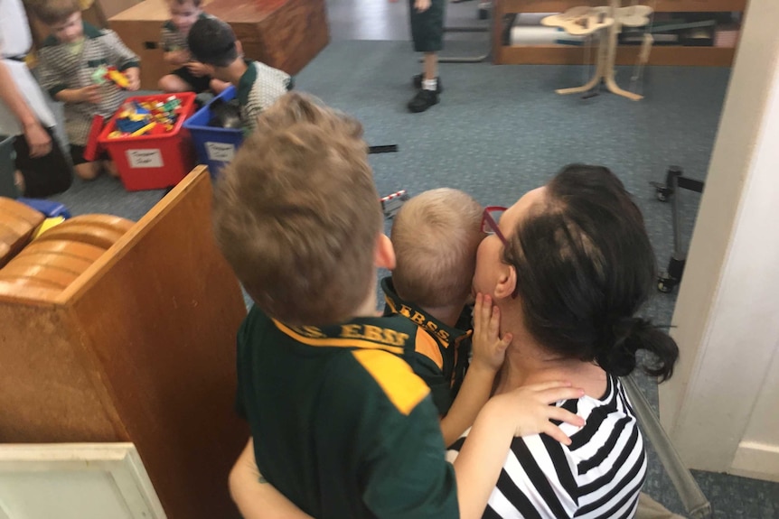 Boys stand with their mum in the classroom.