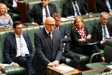a man in glasses with a bald head in a suit delivers a speech to parliament. 
