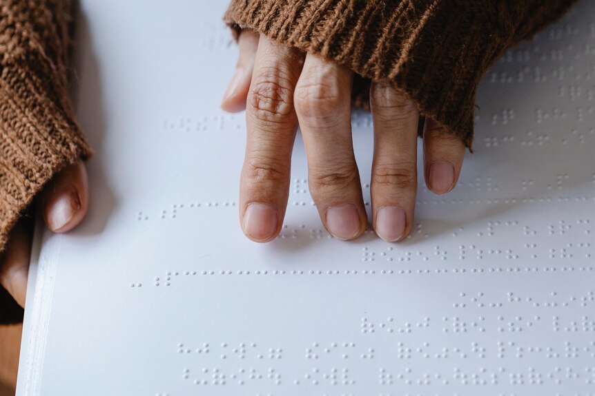 A person wearing a long-sleeved jumper runs their fingers over braille on a page