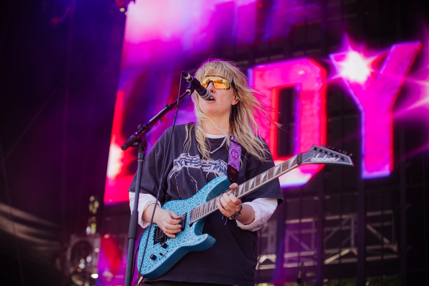 Woman with sunglasses plays guitar on stage