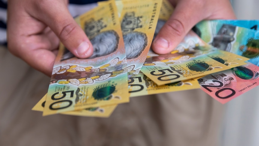 Hands holding 50, 20 and 10-dollar Australian banknotes fanned out