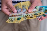 Hands holding 50, 20 and 10-dollar Australian banknotes fanned out