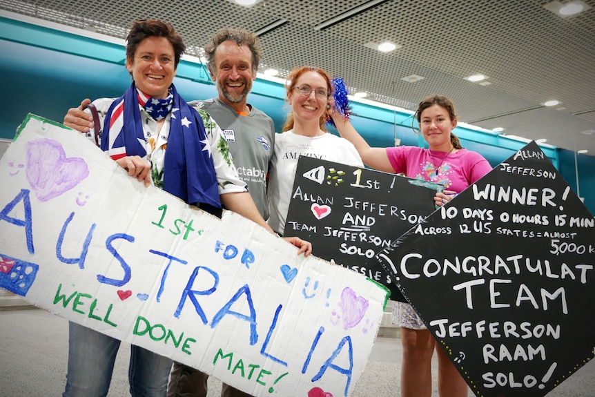 Allan Jefferson poses with three supporters holding signs at the Townsville Airport