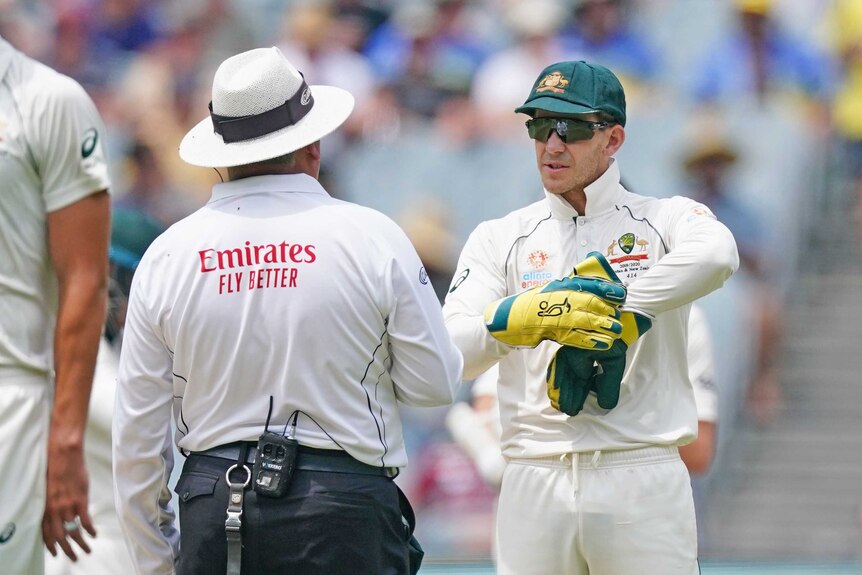 Tim Paine points at his glove in discussion with an umpire