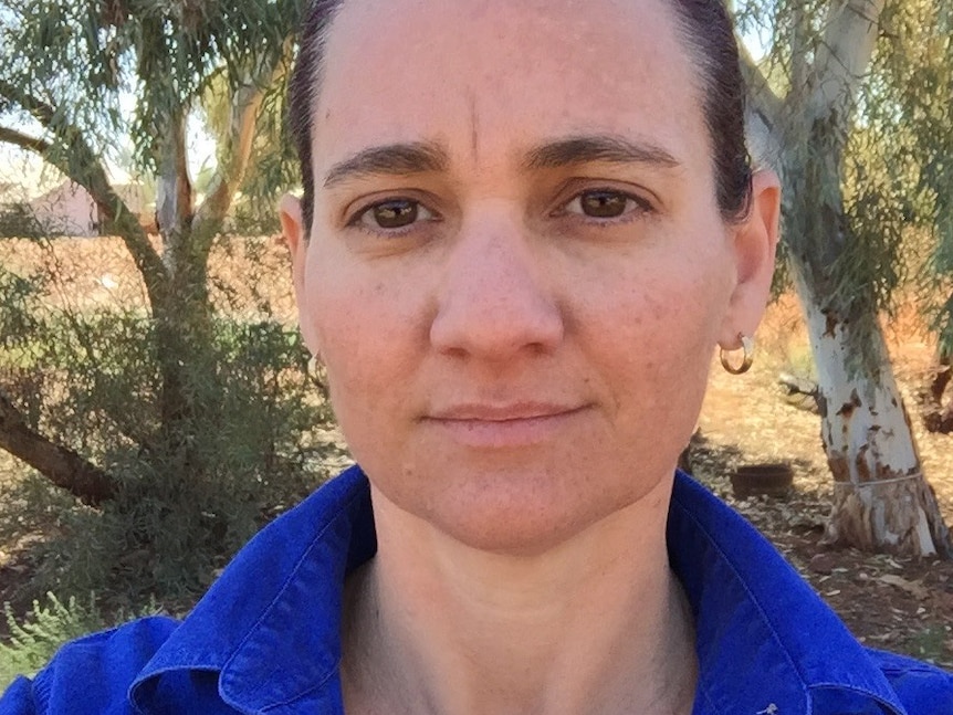 A lady with dark brown hair and eyes looks content wearing a blue work shirt