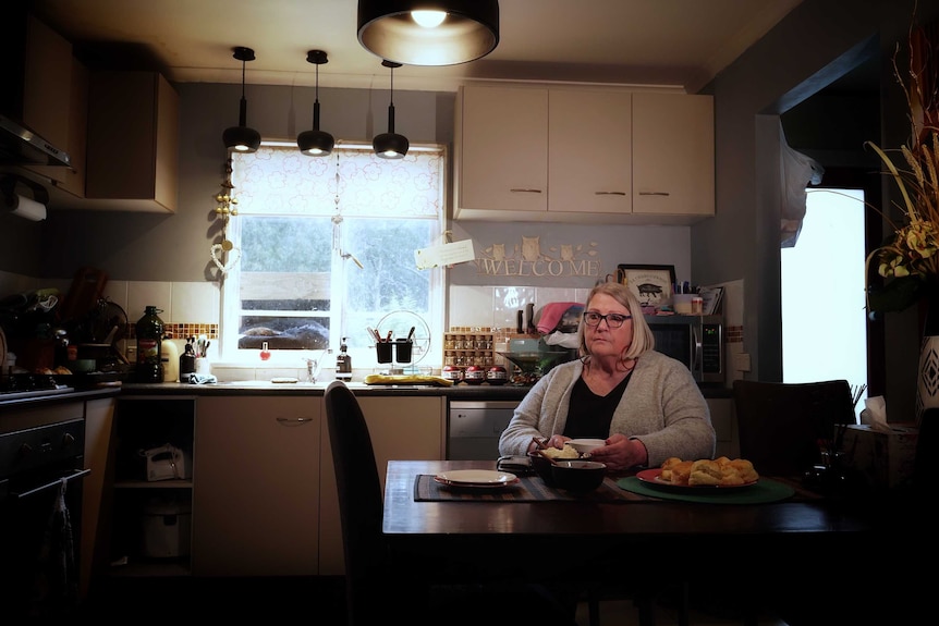 Kathy Flynn sits in her kitchen at a table of scones and holds a cup of tea.