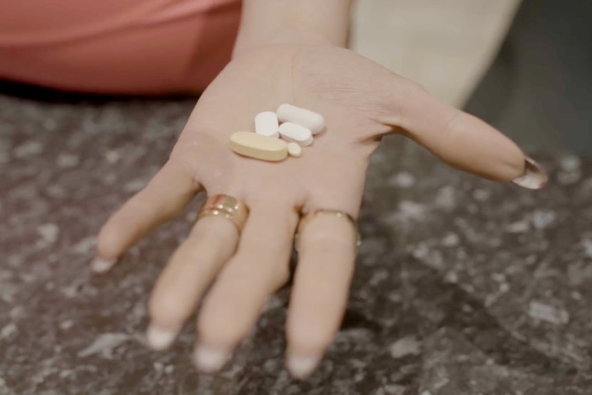 A woman holds five pills in her palm.