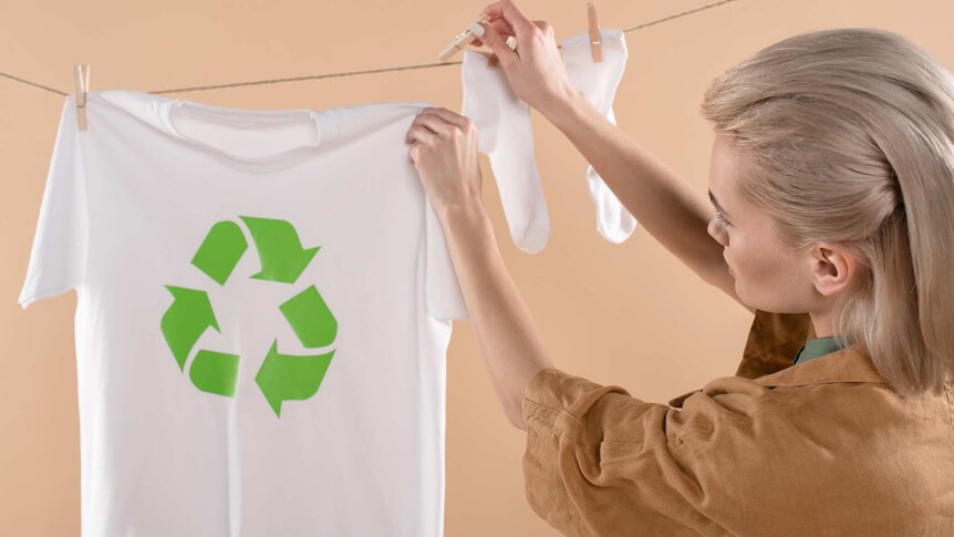 Young blonde woman hanging t-shirt with recycling sign on a clothesline.