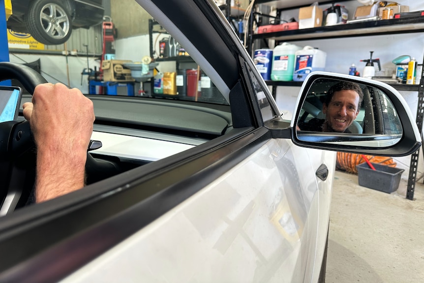 A man smiles in the reflection of a side mirror
