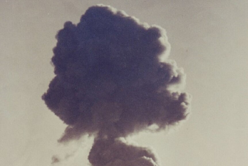 A black and white photo showing a mushroom shaped cloud with a long trail of dust 