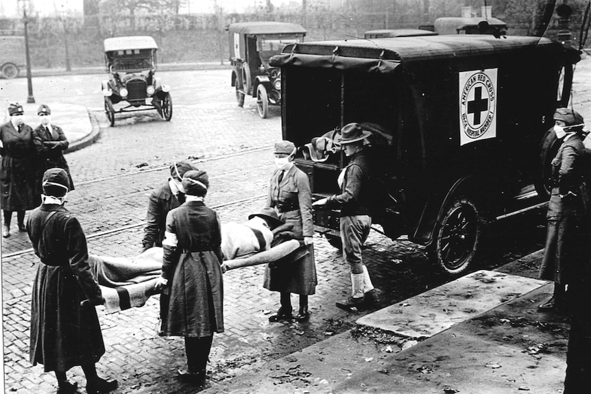 Red Cross Motor Corps women wearing masks carry a patient on a stretcher to an ambulance during the influenza epidemic of 1918.