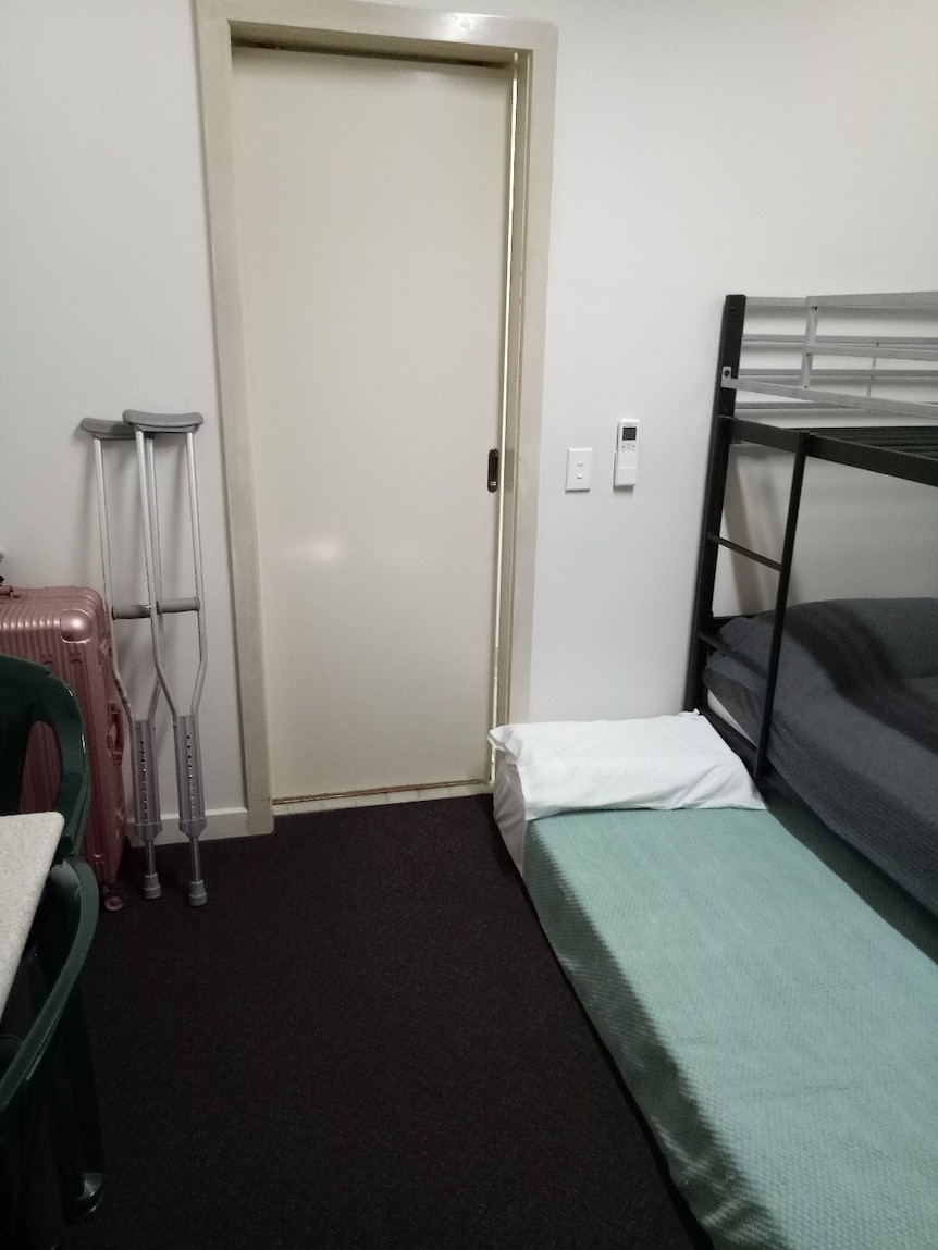 A photograph of Reza Golmohamadian's hotel room with a doorway, floor mattress, bunk bed and crutches in view.