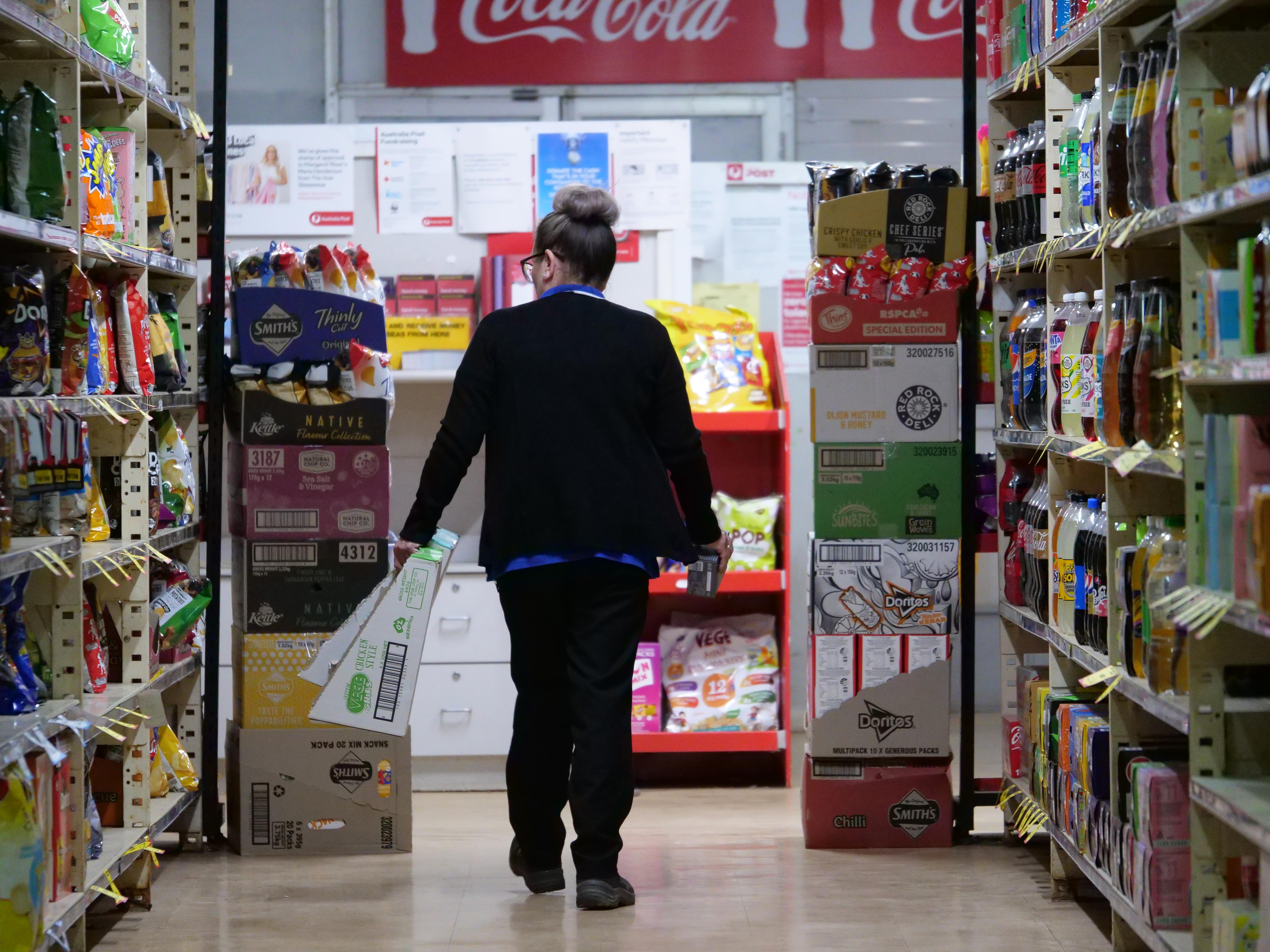 A supermarket employee walking down an isle with food stocked on shelves.  