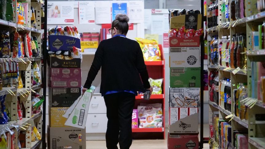 A supermarket employee walking down an isle with food stocked on shelves.  