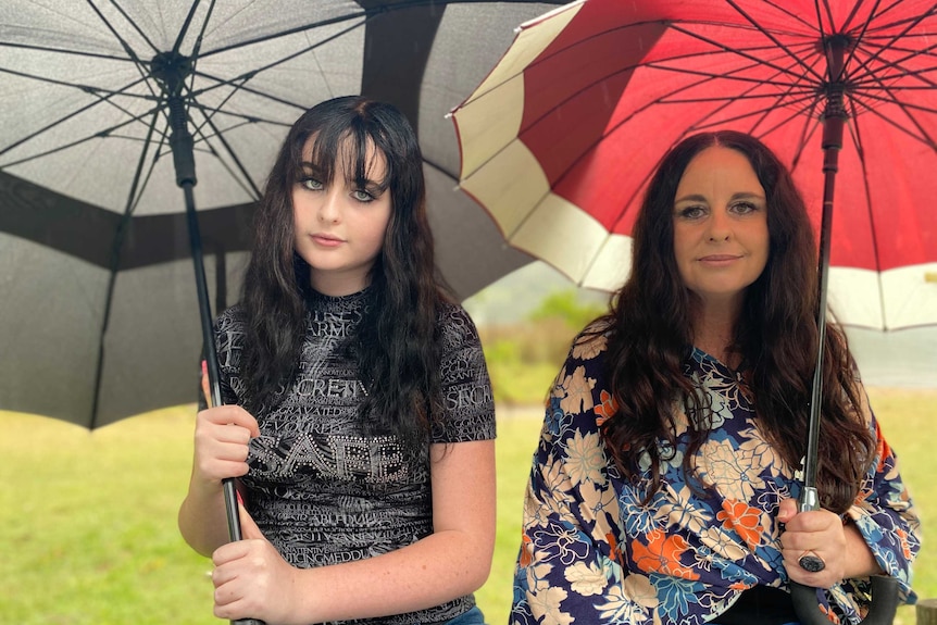 Two women sit under umbrellas in the rain.
