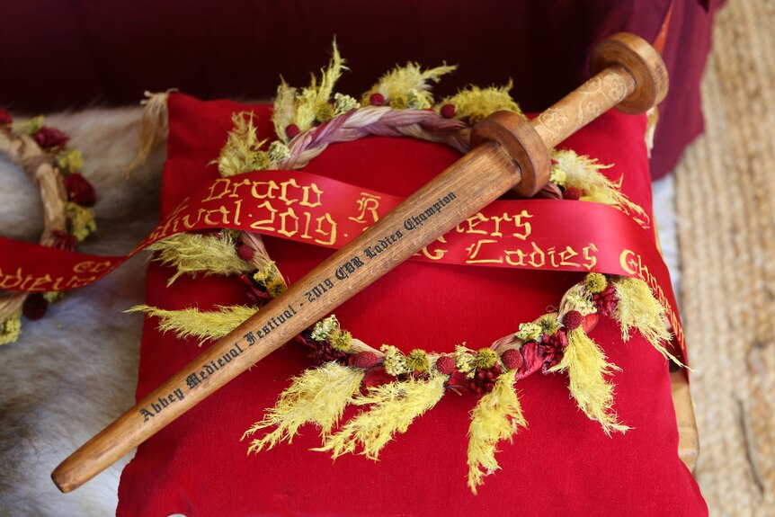 A wooden knife is laid on a ribbon and wreath, on top of a red cushion.