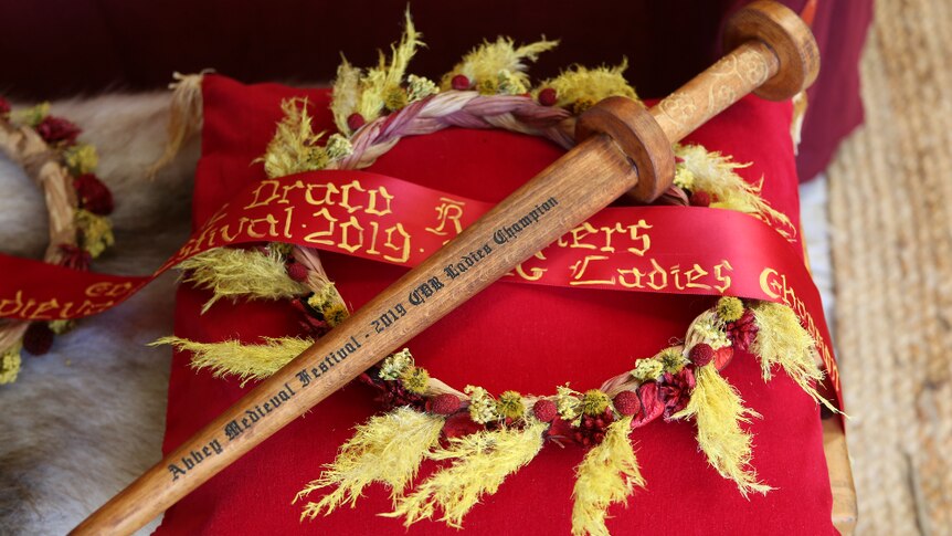 A wooden knife is laid on a ribbon and wreath, on top of a red cushion.