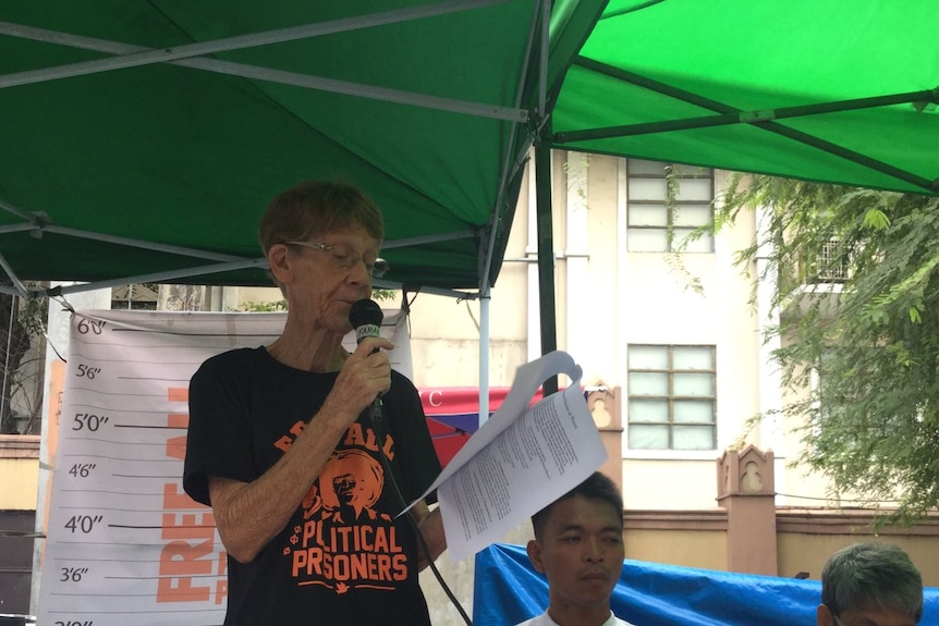 Patricia Fox is giving a speech and wearing a t-shirt printed with "free all political prisoners".