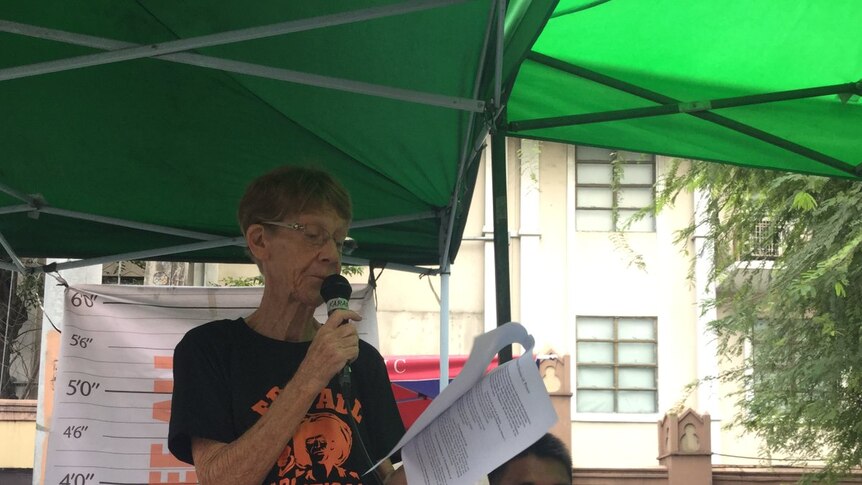 Patricia Fox is giving a speech and wearing a t-shirt printed with "free all political prisoners".