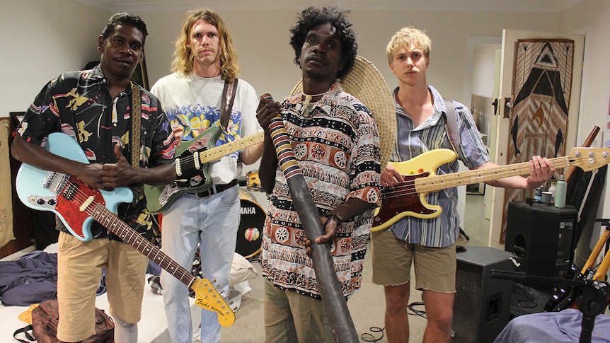 Four members of King Stingray holding their instruments in a band practice room