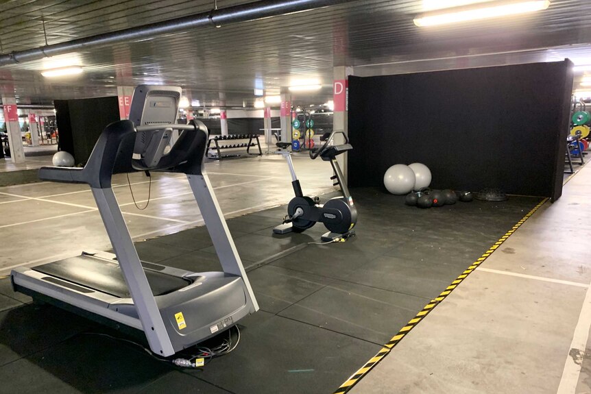 A treadmill and an exercise bike are spaced several metres apart in a large underground car park.