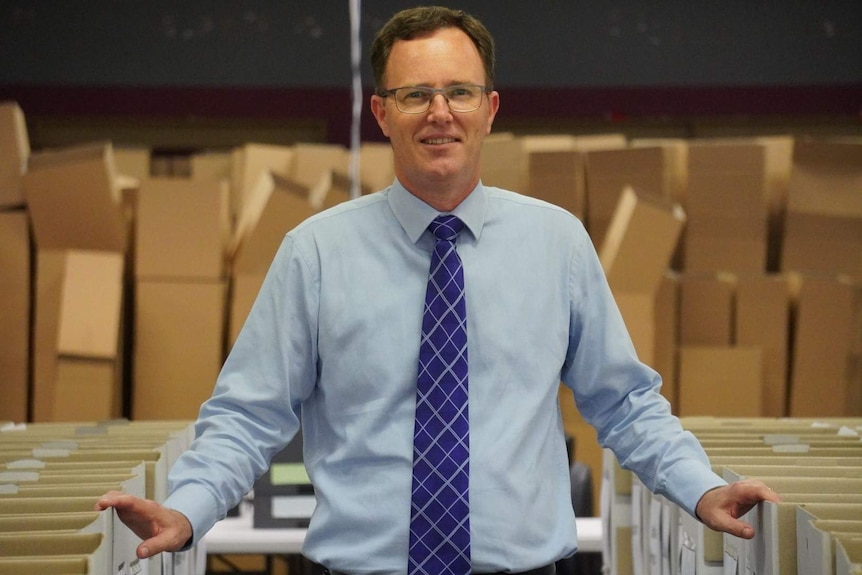 A photo of WA Electoral Commissioner Robert Kennedy standing between rows of empty boxes.