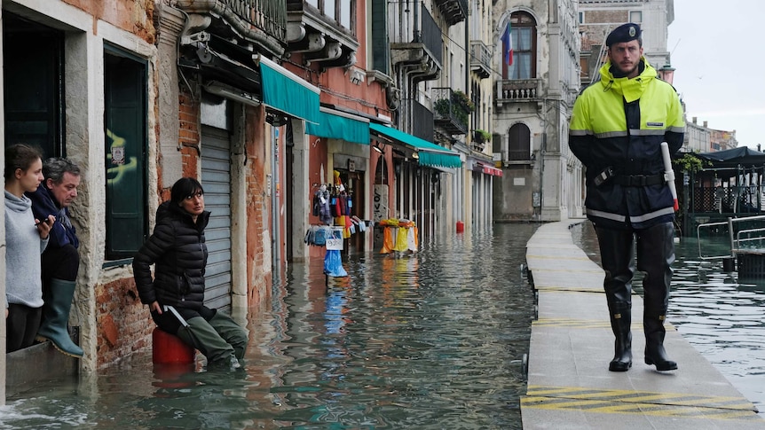 A policeman walks on a temporary walkway above a flooded street as people watch him.