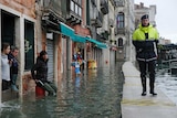 A policeman walks on a temporary walkway above a flooded street as people watch him.