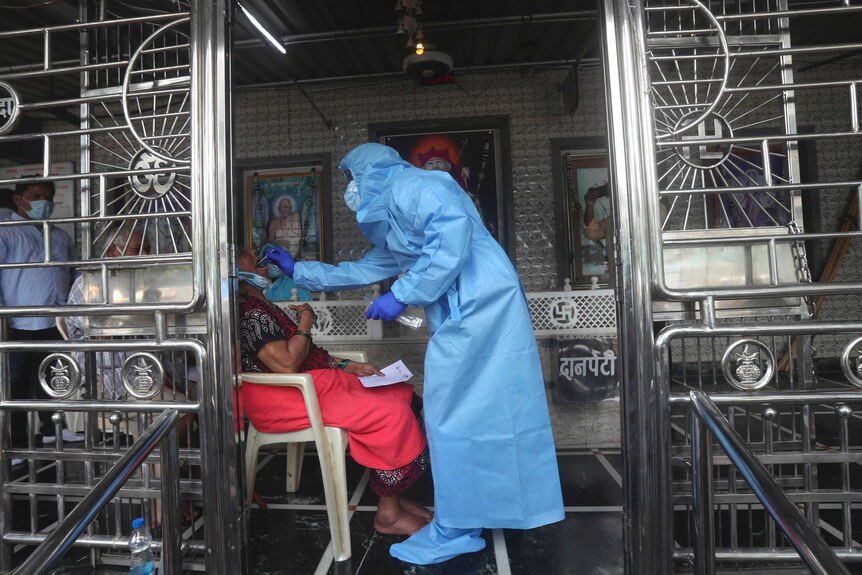 A health worker in full PPE takes a swab from the mouth of an older woman.