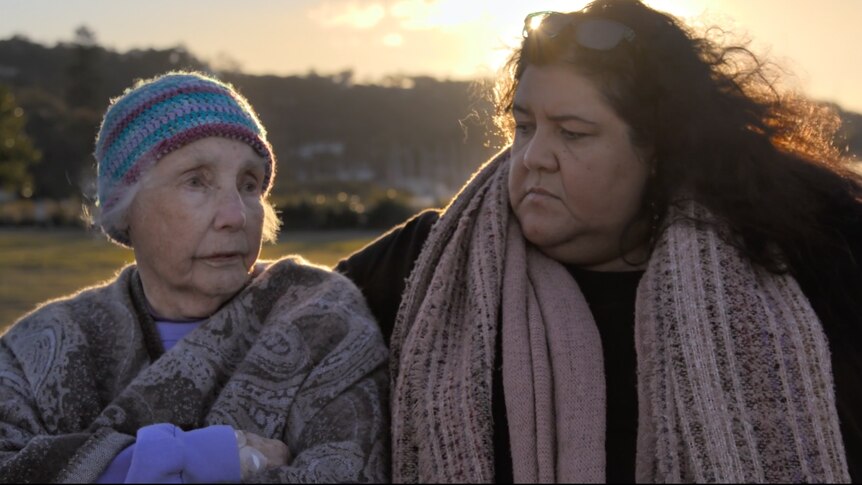 Head and shoulders image of an older woman and a younger woman sitting side by side outside, sharing a feeling.