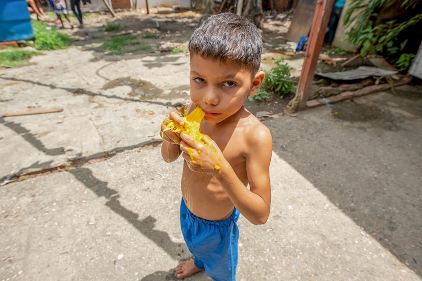 A little shirtless boy eating a mango
